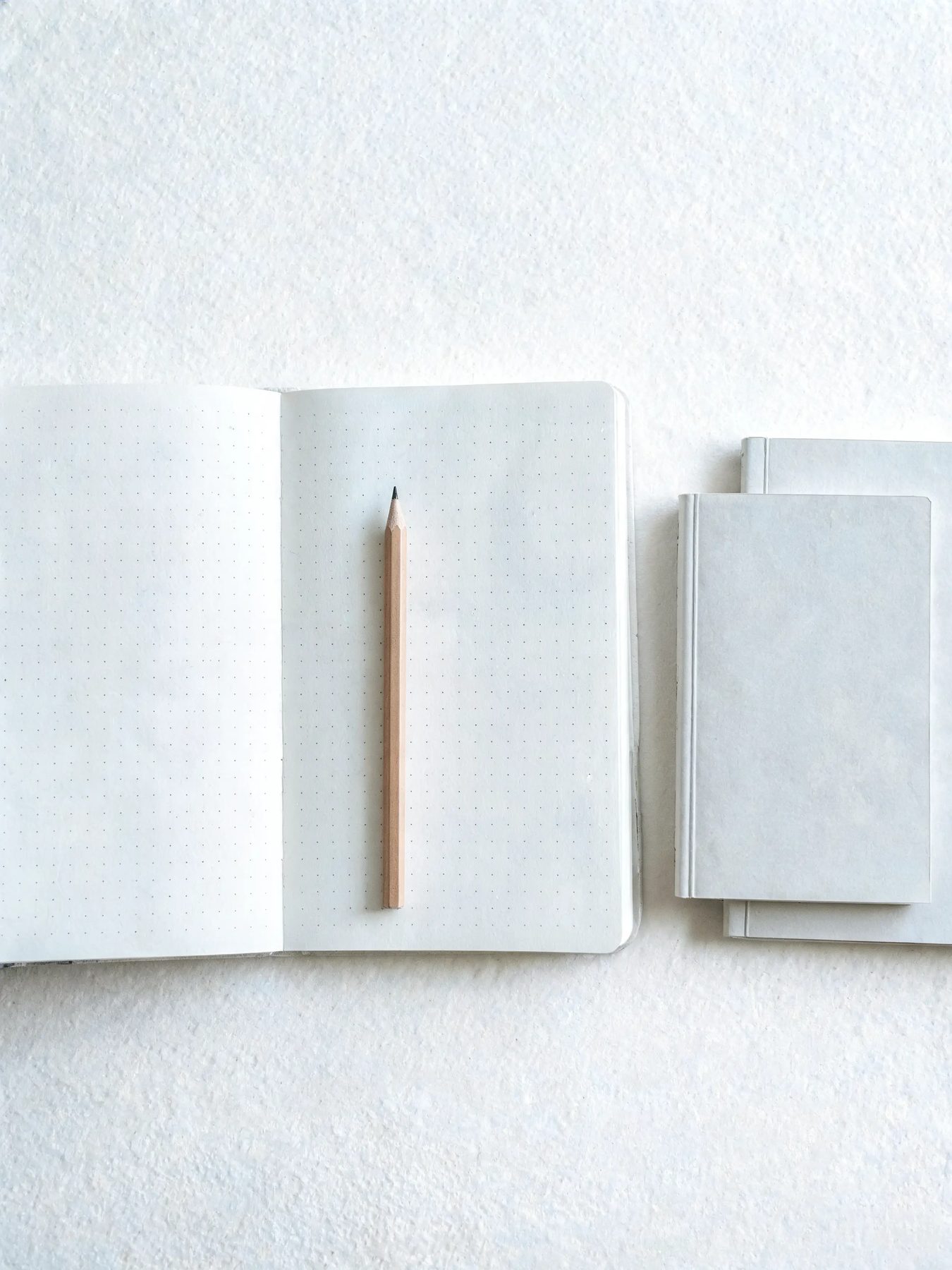 Open dotted notebook with a graphite pencil and two pocket books stacked beside it